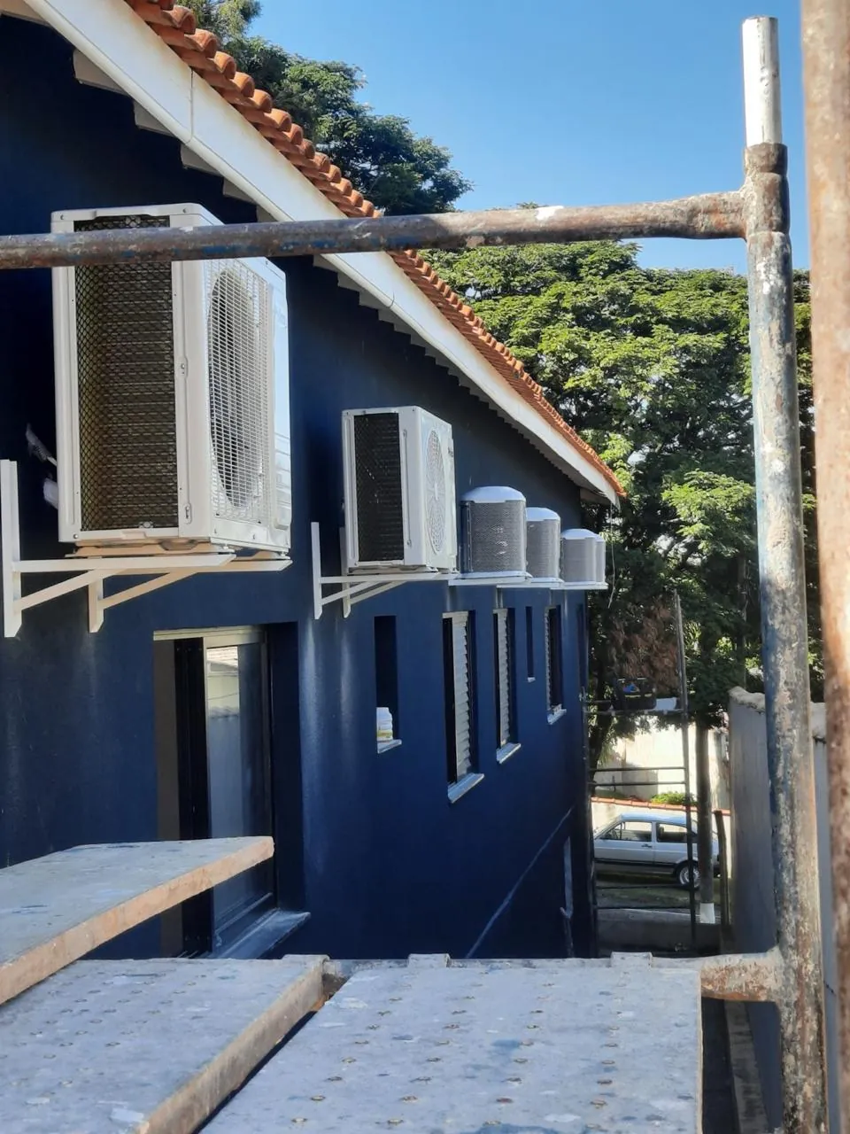 Condensadoras fixadas em suportes na fachada azul, vistas pela lateral.